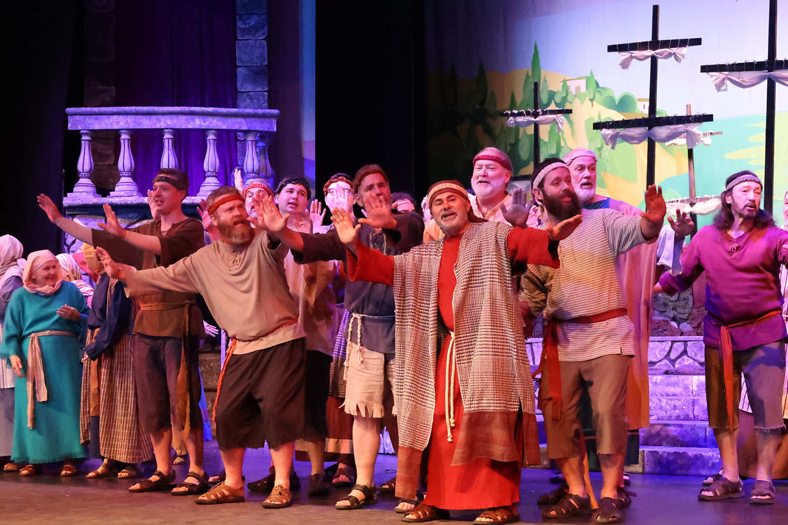 A crowd sings in a biblical seashore setting.